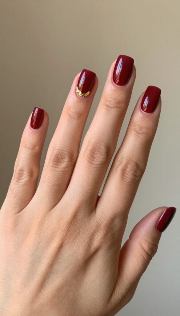 Square medium nails in cranberry red with gold foil accents on ring finger