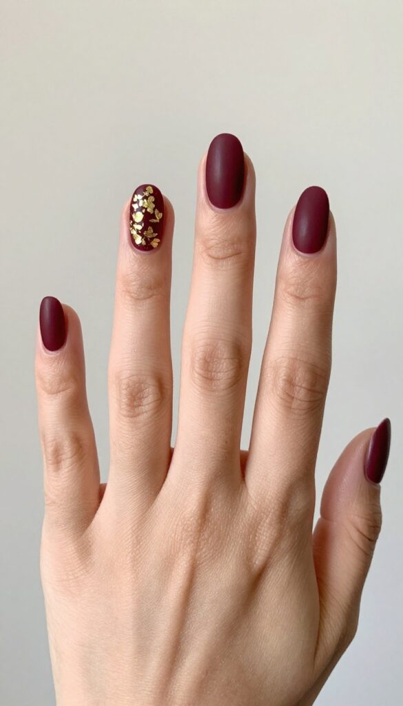 Matte merlot nails with gold foil accents on ring finger
