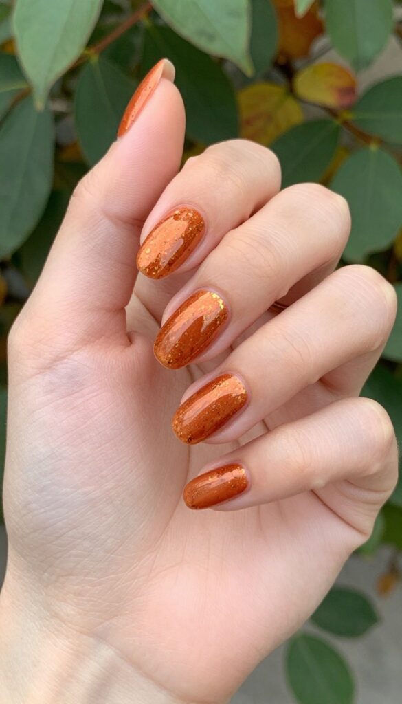 Copper chrome nails with gold speckles on almond-shaped nails