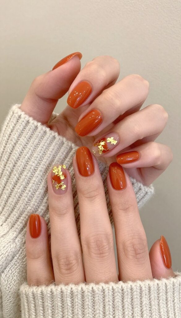 Burnt orange gel nails with gold foil accents, almond shape, glossy finish, autumn manicure