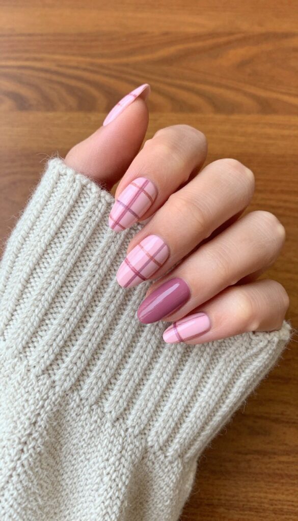 Pink plaid nail design on almond-shaped nails with pale pink base and mauve and rose gold lines, resting on a knit sweater.