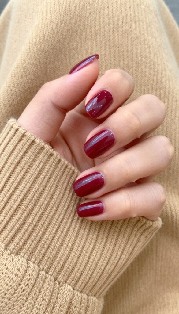 Cranberry red glossy nails on a woman's hands resting on a sweater