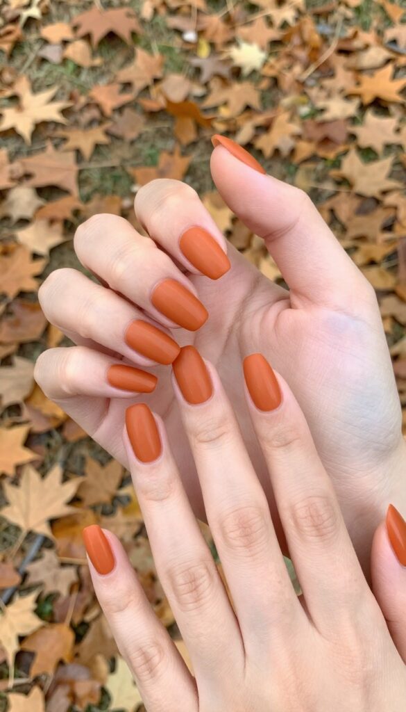 Burned orange matte almond nails on a woman's hand in an autumn setting