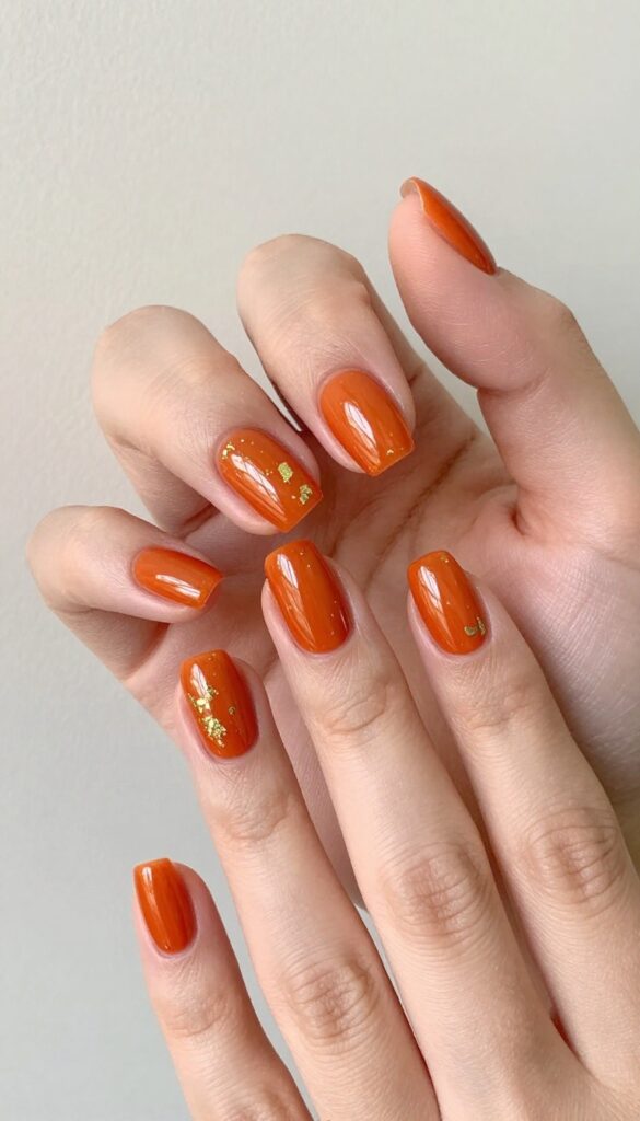 Burnt orange coffin nails with gold foil accents on a woman's hand
