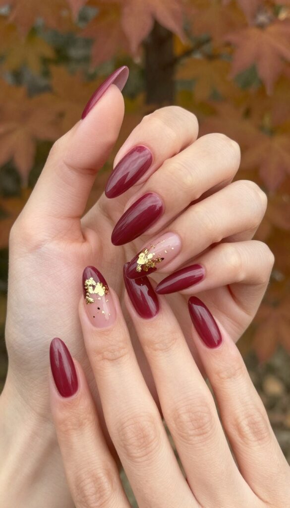 Burgundy stiletto nails with gold foil accents on a woman's hand