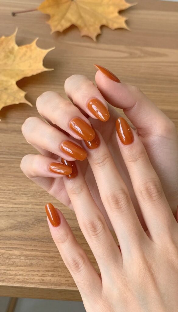 Glazed gingerbread orange acrylic nails with glossy finish on a woman's hand in an autumn setting