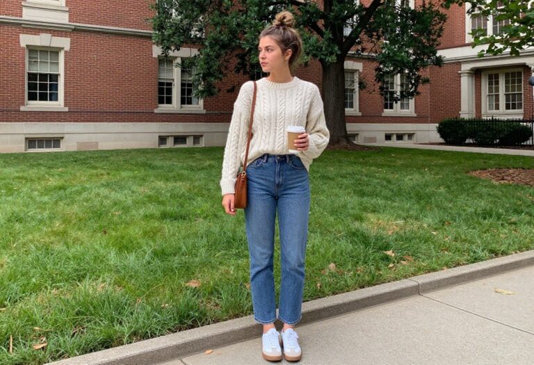 College girl in cream sweater and jeans on campus with coffee
